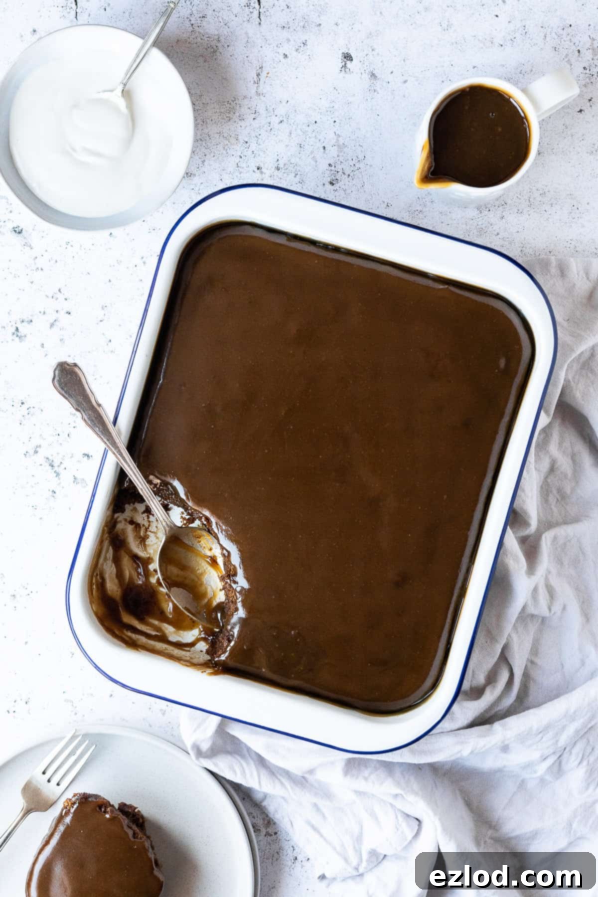 Vegan sticky toffee pudding in an enamel dish with a spoonful scooped out onto a plate.