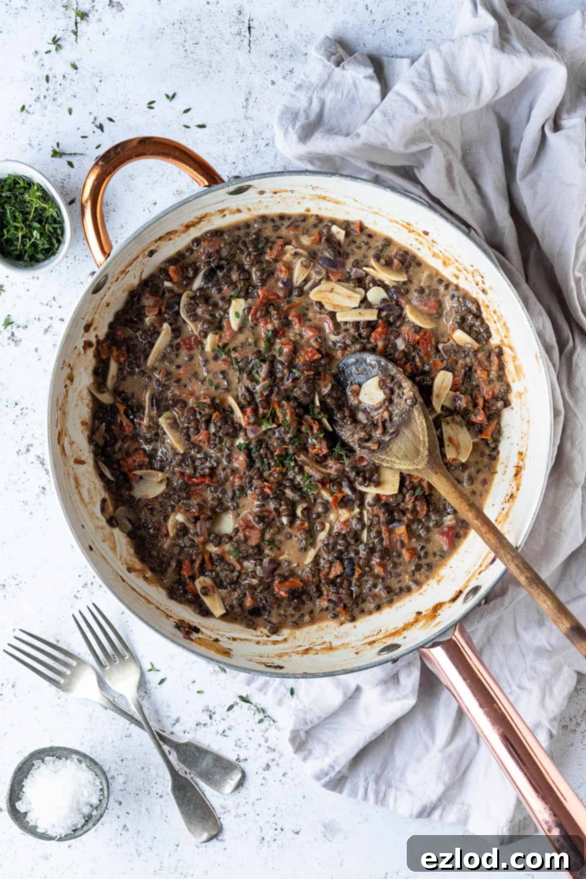 A close-up view of the rich, creamy sun-dried tomato puy lentil sauce simmering in a white pan, showing its vibrant color and thick texture before the pasta is added.