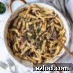 A white pan full of sun dried tomato puy lentil pasta on a white surface with a grey cloth, two forks, bowl of salt and bowl of thyme leaves.