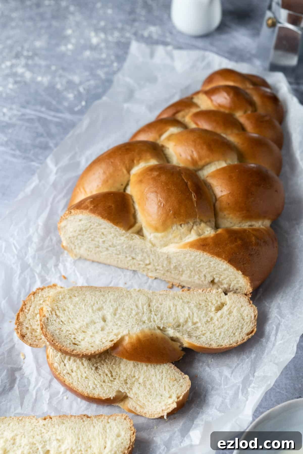 A perfectly sliced vegan pulla loaf rests on white baking parchment on a metal surface, showing off its beautiful texture and golden crust, ready to be served.