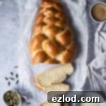 Sweet Vegan Cardamom Braid 8 A freshly baked vegan pulla bread, with three delicious slices cut, presented on a sheet of baking parchment. The scene includes cardamom pods, plant-based milk, a pastry brush, coffee, and a French press, evoking a warm, inviting breakfast setting.
