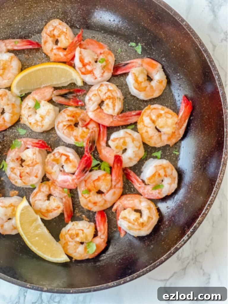 Overhead photo of cooked shrimp in a pan with lemon slices and parsley
