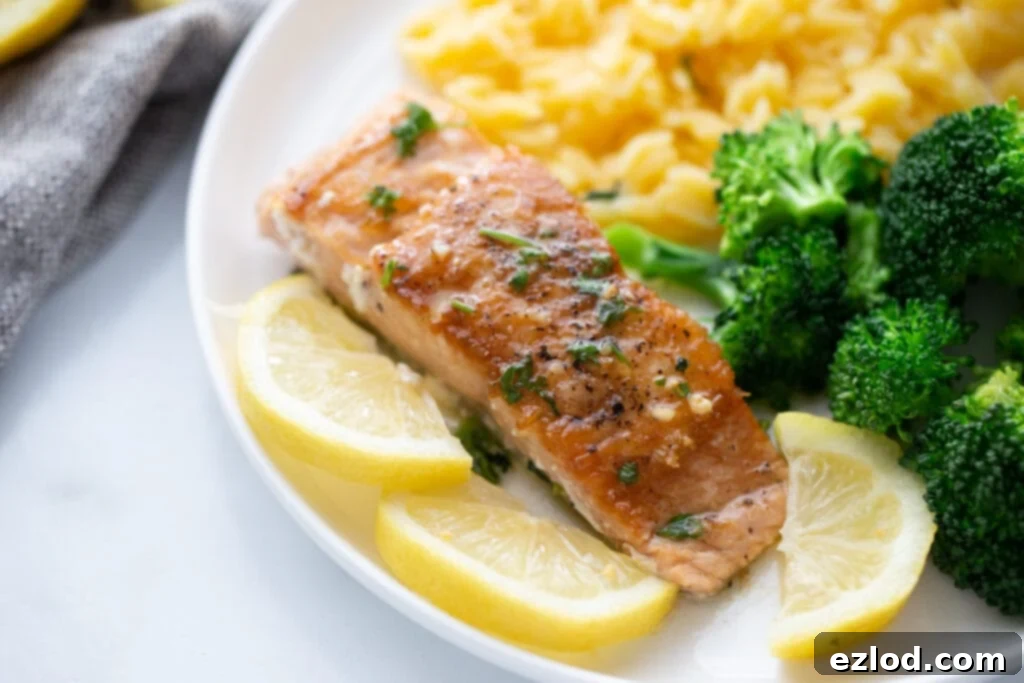 Pan seared salmon on a white plate with sliced lemons and sides of broccoli and gluten free orzo, showcasing a crispy texture.