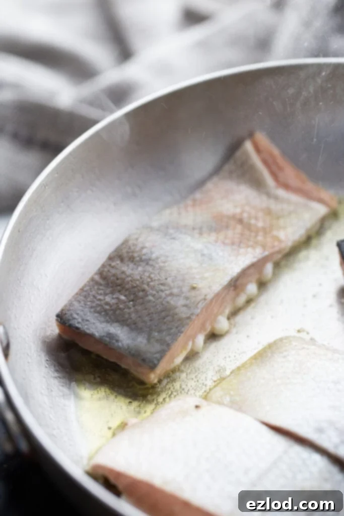 Salmon cooking flesh-side down in a stainless steel pan, showing early stages of crust formation.