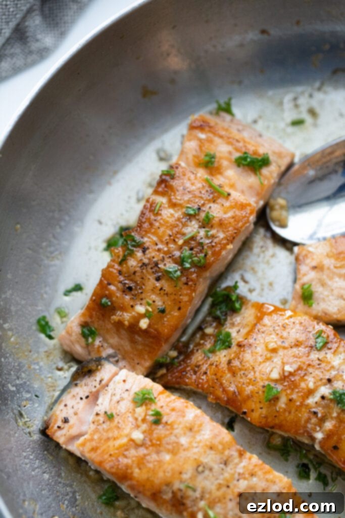 Crispy salmon finished with butter and garlic sauce in a stainless pan, demonstrating the final flavorful step.
