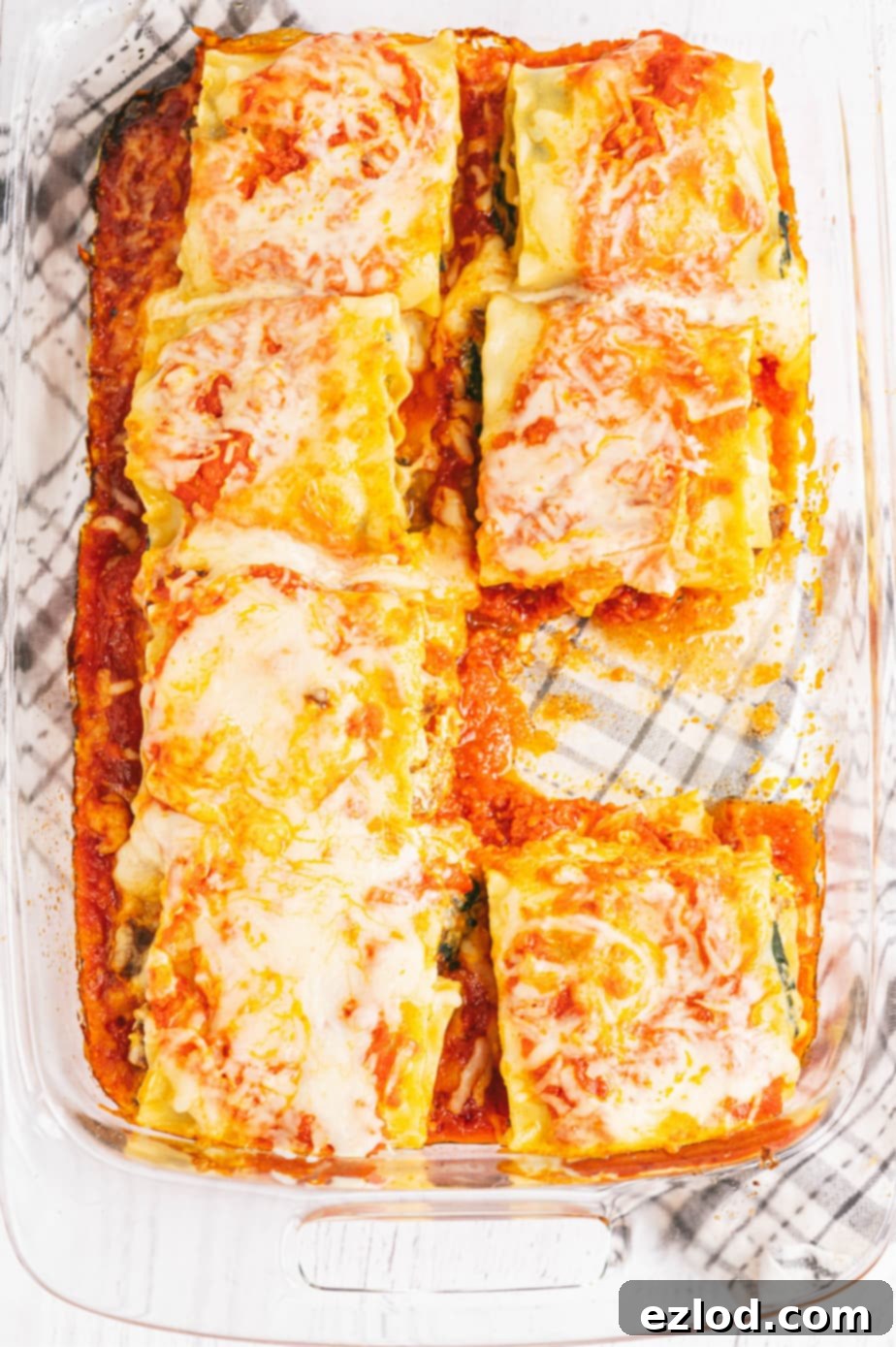 Freshly baked lasagna roll ups in a casserole dish, topped with melted mozzarella and simmering marinara sauce.