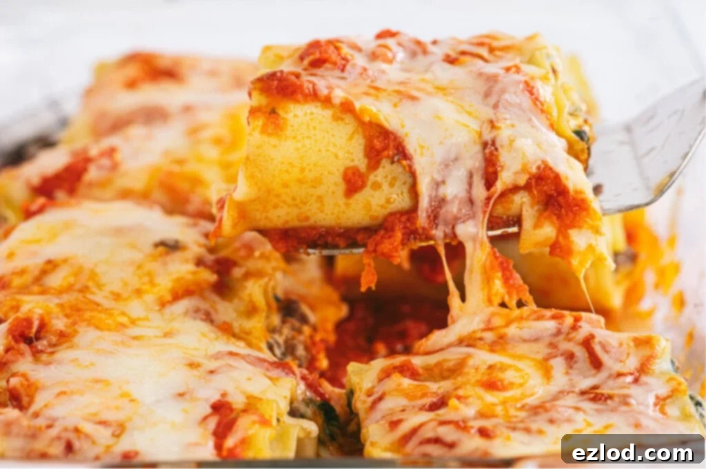 Close-up photo of a serving spatula lifting a single lasagna roll out of a baking dish, with strings of gooey melted cheese stretching from the dish.
