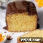A top-down view of a vegan orange loaf cake with a generous chocolate glaze, garnished with orange zest.