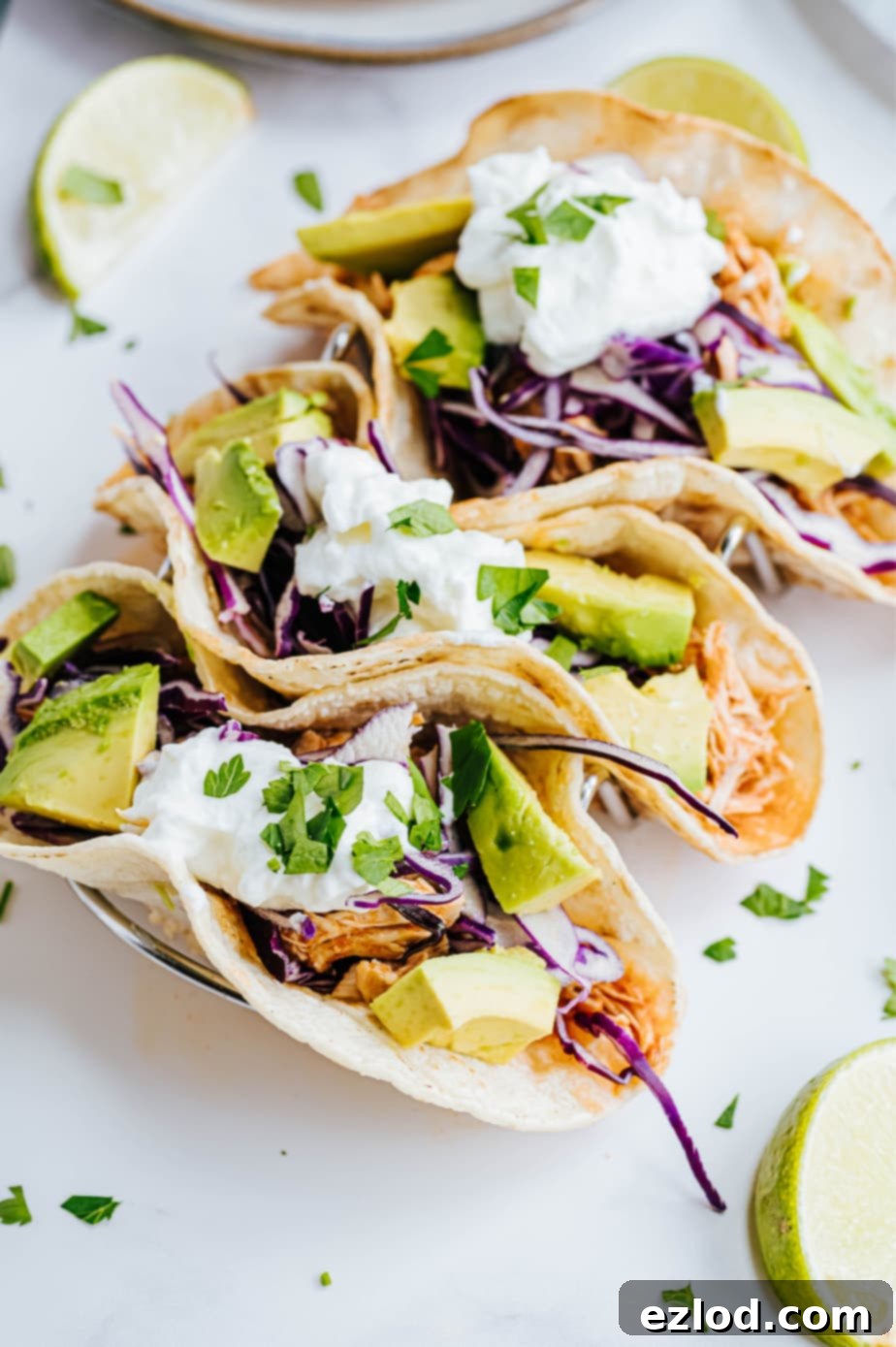 Ultimate Instant Pot Chicken Tacos 2 A close up shot reveals multiple fresh veggies garnishing three Instant Pot chicken tacos, showing colorful toppings like purple cabbage, avocado, and cilantro.