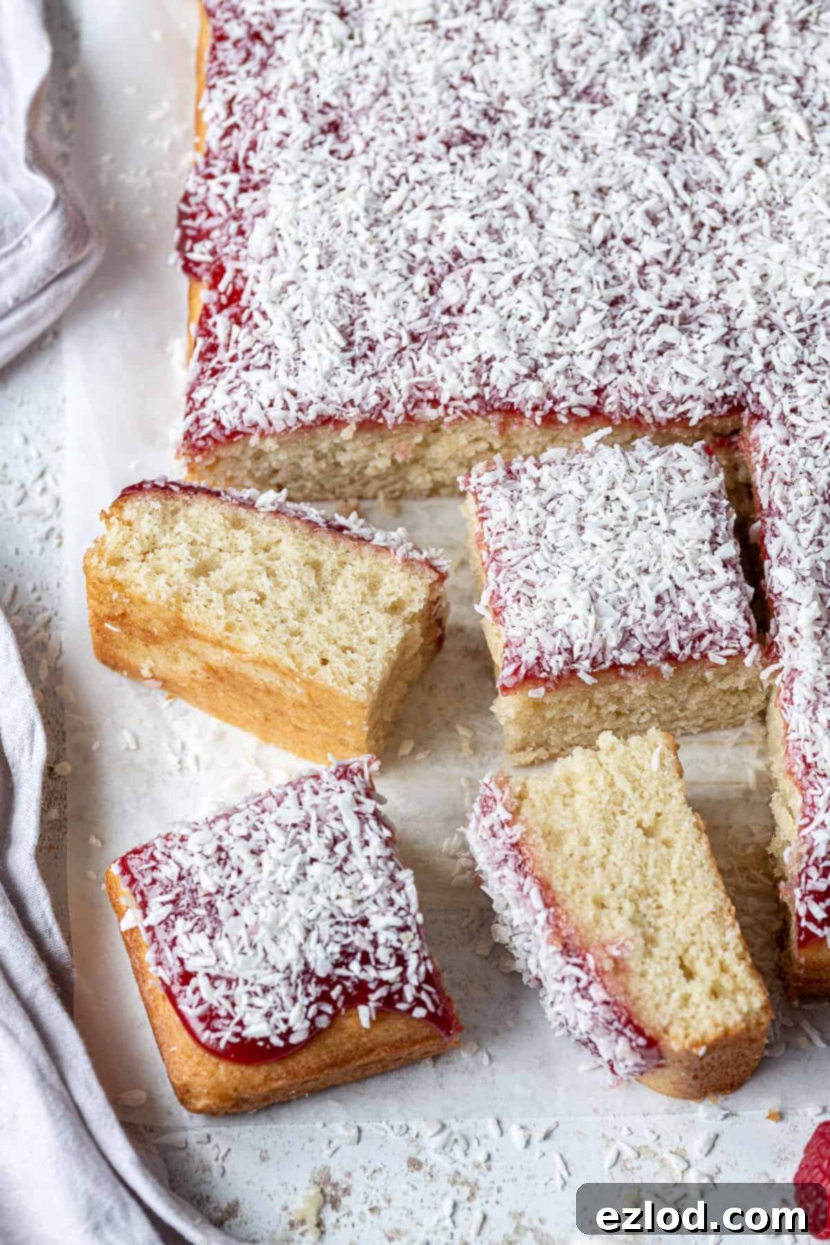 Slices of vegan jam and coconut sponge cake on a sheet of baking parchment.