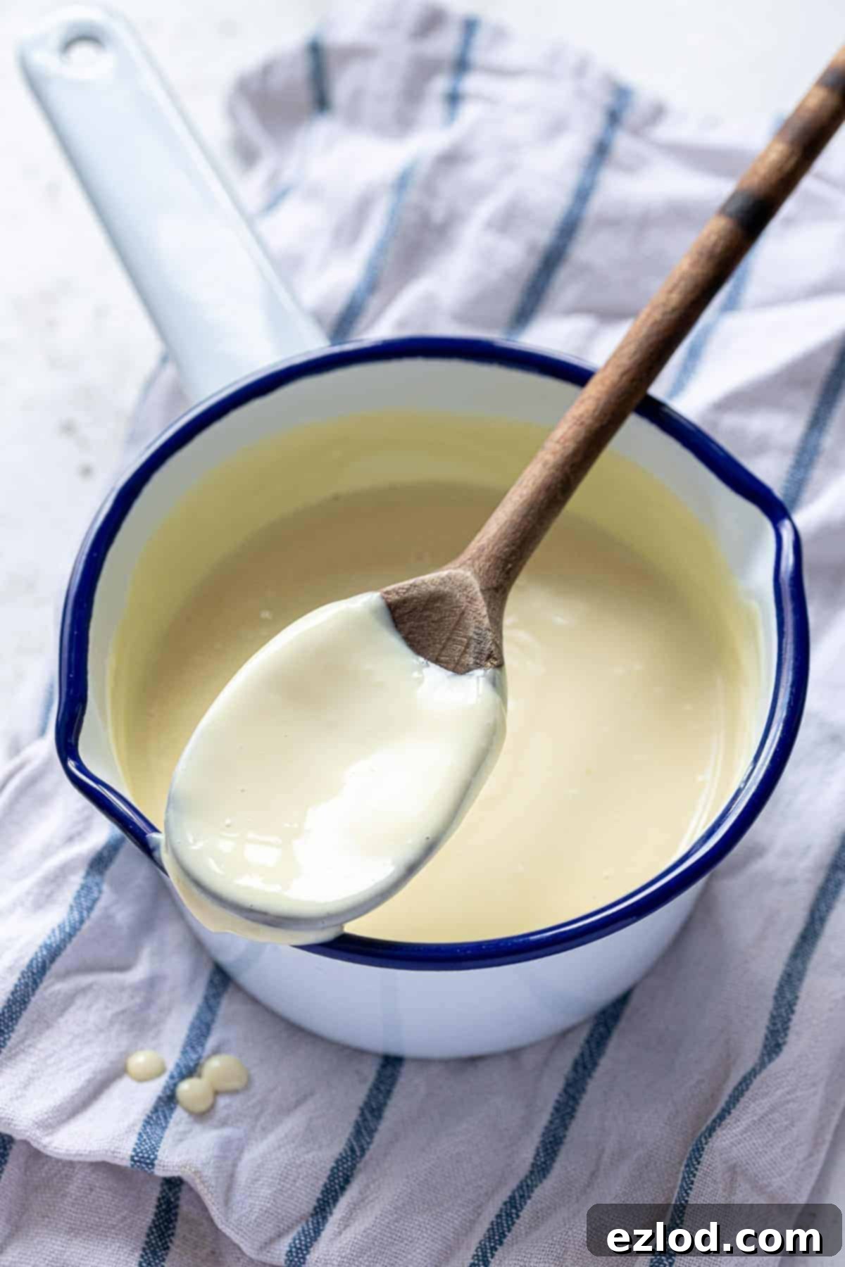 Vegan vanilla custard simmering gently in a rustic blue and white enamel pan, with a wooden spoon resting on the edge, ready to serve.