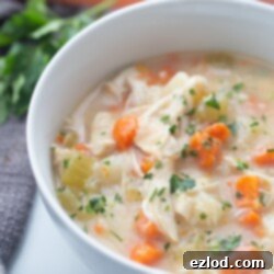 Homestyle Chicken Pot Pie Soup 12 A white bowl containing healthy Instant Pot chicken pot pie soup is placed on a white surface with blurred carrots in the background.