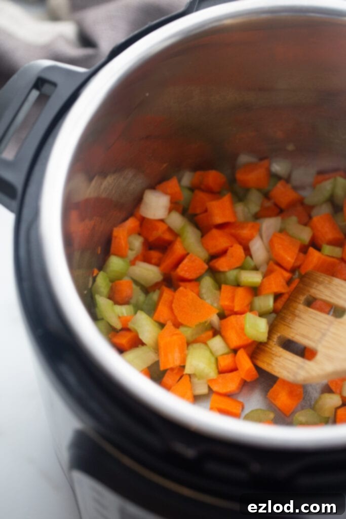 Diced carrots, onions, and celery are actively sautéing in the Instant Pot, forming the flavorful aromatic base for the chicken pot pie soup.
