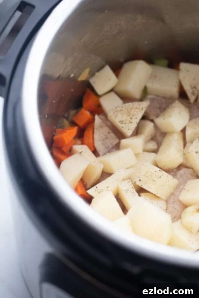 Diced potatoes and carrots are placed inside the Instant Pot, layered with chicken, ready for the broth and cauliflower.