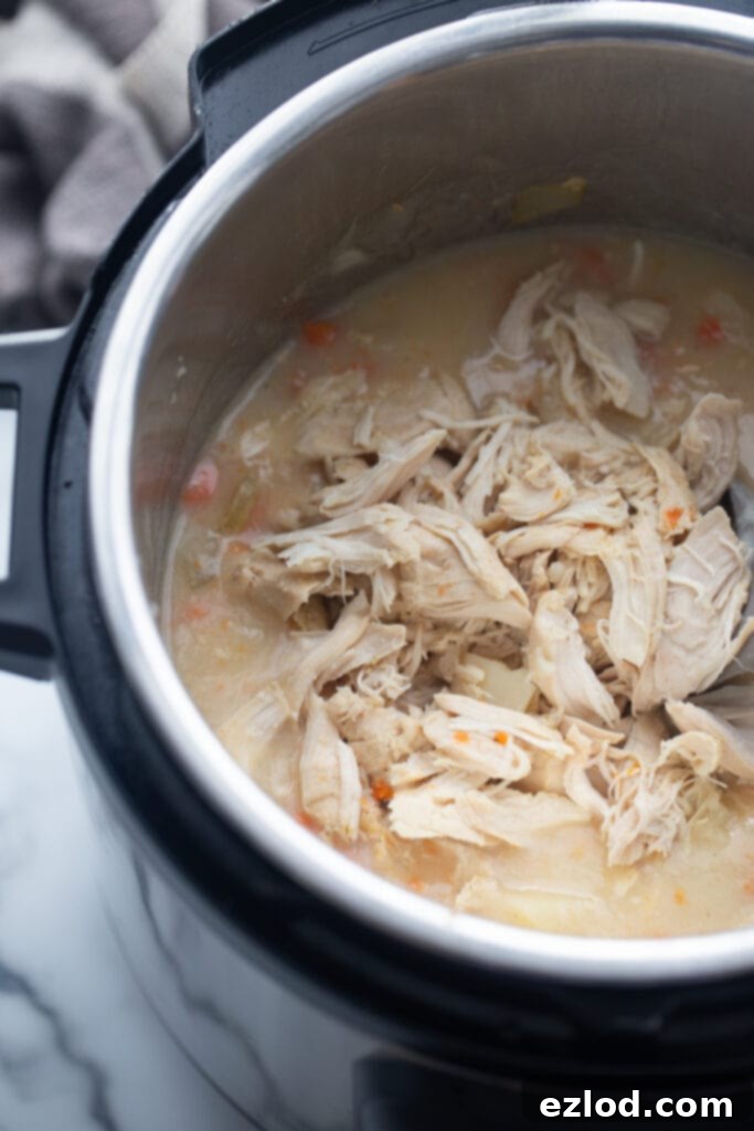Shredded chicken pieces are visible inside the Instant Pot, ready to be mixed back into the savory chicken pot pie soup.