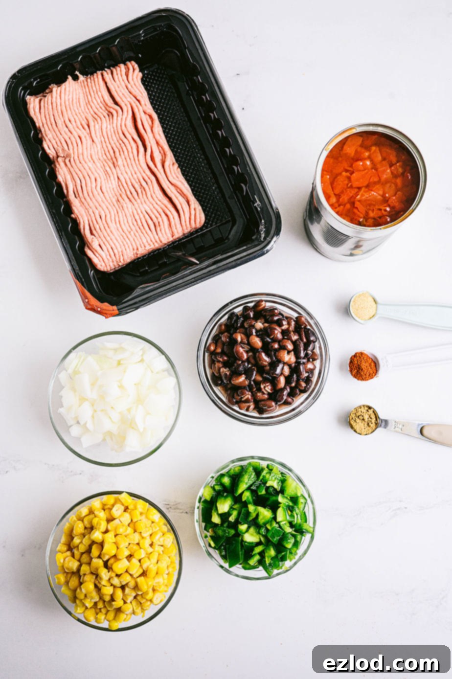 Overhead shot of fresh ingredients for the turkey taco skillet, including raw ground turkey, canned tomatoes, black beans, frozen corn, diced onions, and bell peppers.