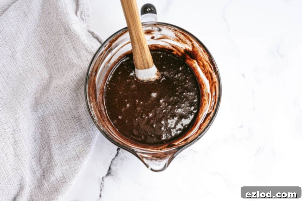 Glass liquid measuring cup with homemade brownie batter and a rubber spatula, ready for baking.