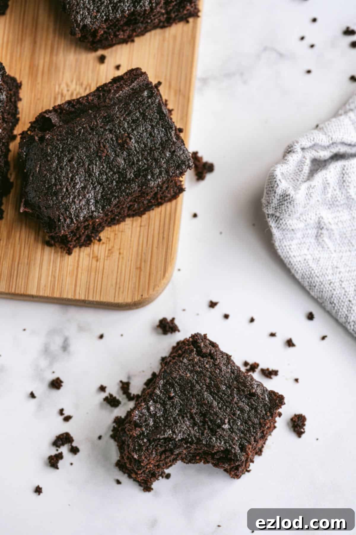 Homemade brownies on a wooden cutting board with scattered crumbs, indicating their deliciousness.