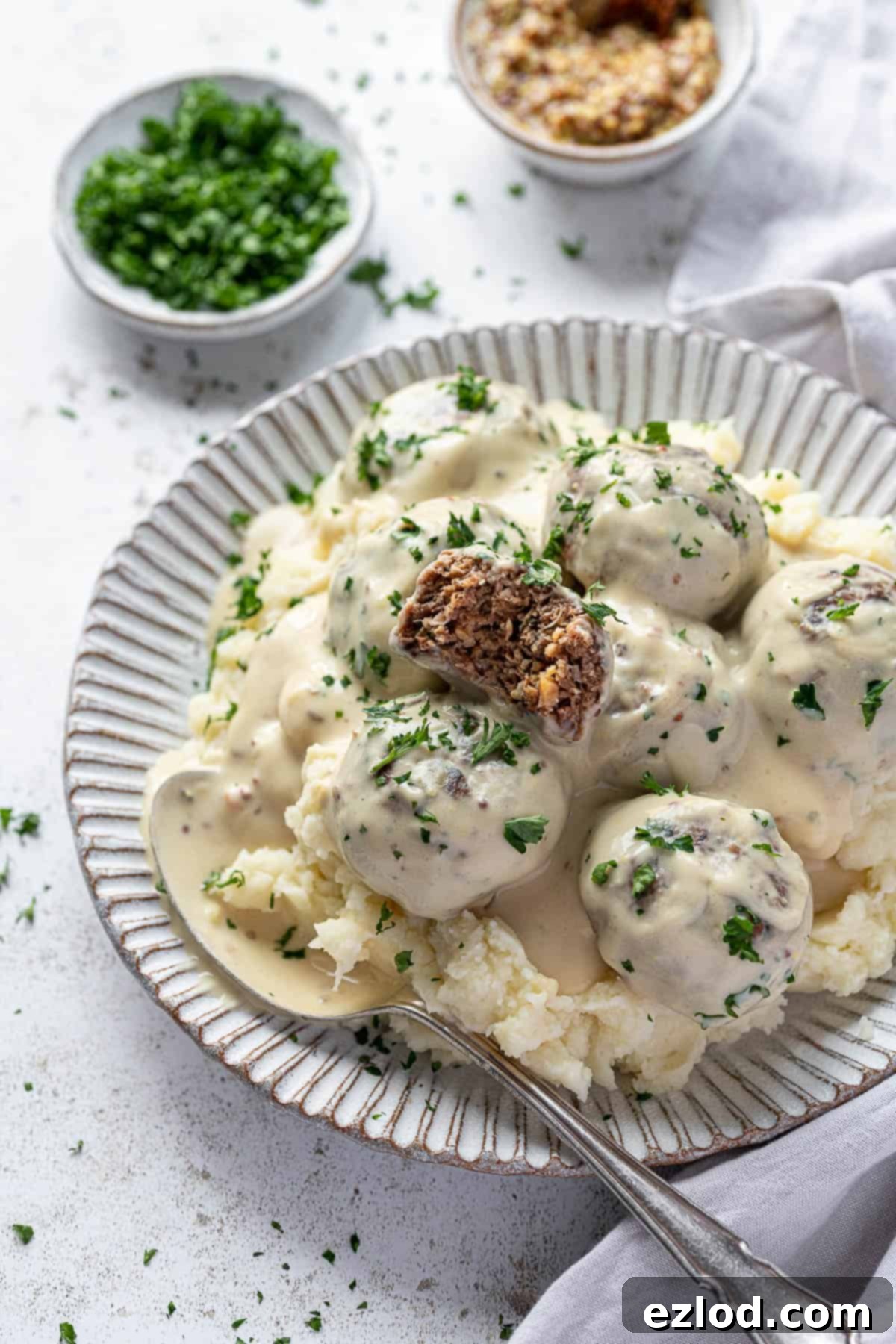 Vegan Swedish meatballs and mashed potato on a white plate with a bowl of parsley and a bowl of mustard.