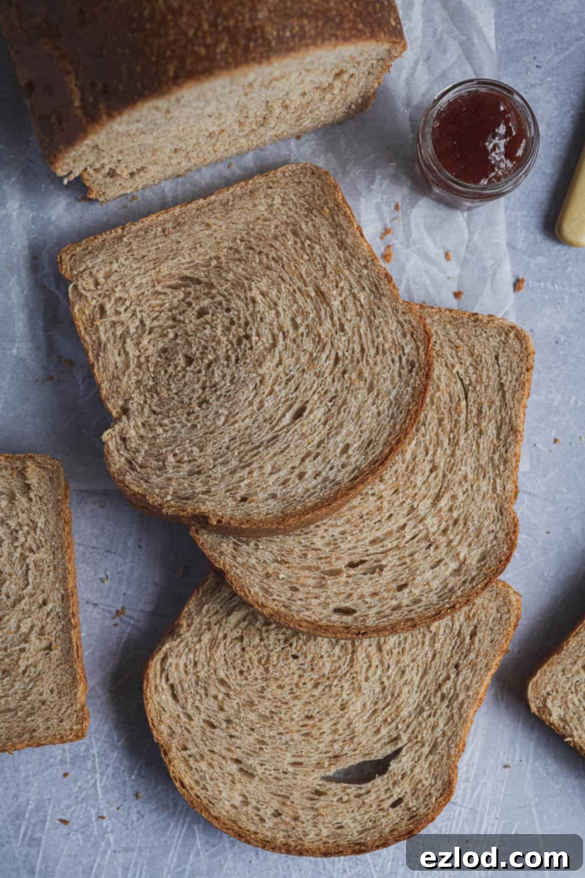 A charming display of slices of vegan wholemeal sandwich bread, accompanied by a jar of vibrant jam, ready for enjoyment.