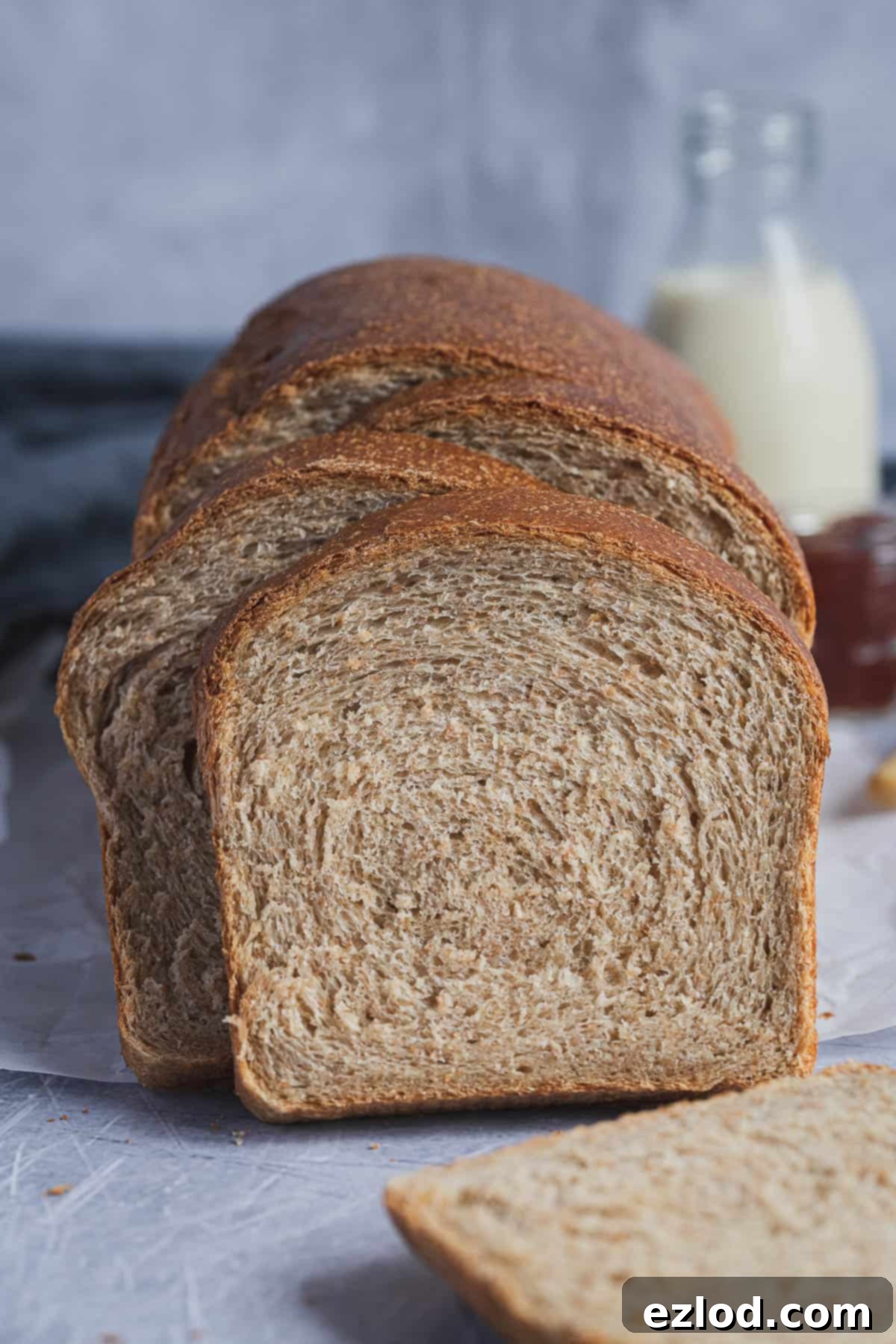 Close-up of perfectly sliced vegan wholemeal sandwich bread, revealing its tender crumb, with a bottle of plant-based milk in the background.