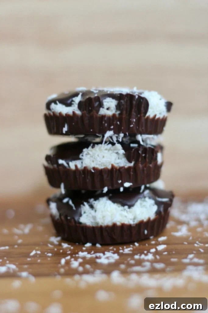 Close up side view of a stack of 3 homemade chocolate coconut cups- copycat mounds candy. There is coconut sprinkled on the wooden tabletop.