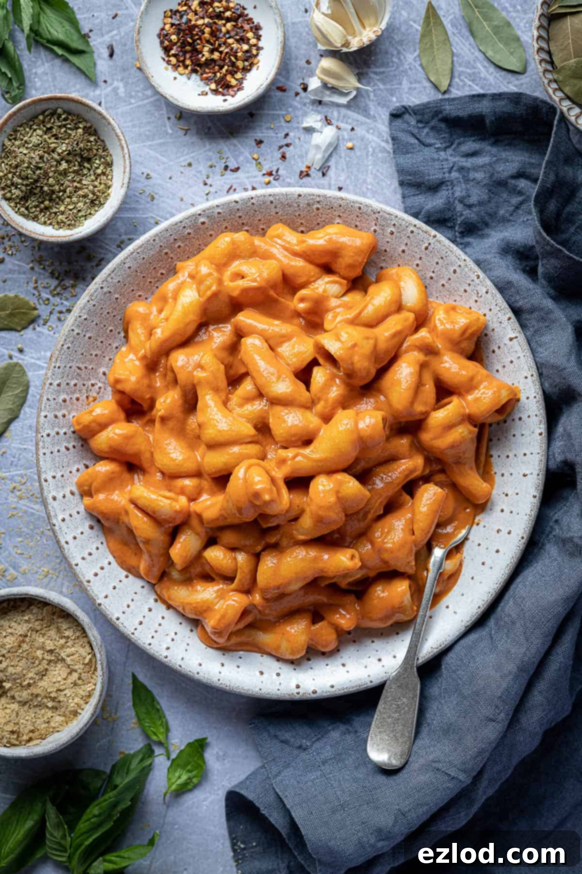 A mouthwatering bowl of pasta generously coated with creamy tofu tomato sauce, beautifully garnished with fresh herbs, ready to be enjoyed.