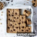 Vegan oatmeal cookie bars in a parchment lined metal tin with a bowl of walnuts and a bowl of chocolate.