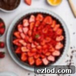 Vegan chocolate strawberry tart on a white serving plate with bowls of strawberries, chocolate pastry cream, chocolate shavings and apricot jam glaze.