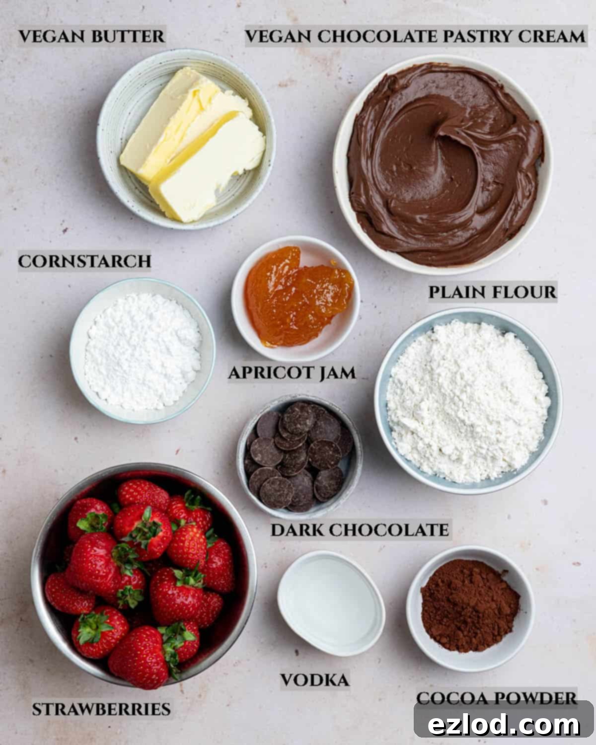 A vibrant flat lay photo showcasing all the fresh and dry ingredients required to prepare the vegan chocolate strawberry tart, neatly arranged and labelled.
