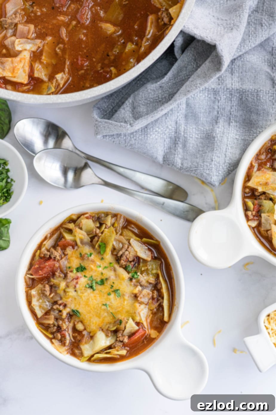 Two white bowls filled with unstuffed cabbage roll soup are on a white surface, ready to be served.
