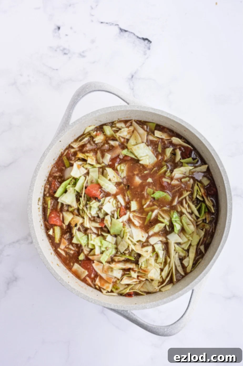 A large white pot contains the stirred ingredients for unstuffed cabbage roll soup, simmering on the stovetop.