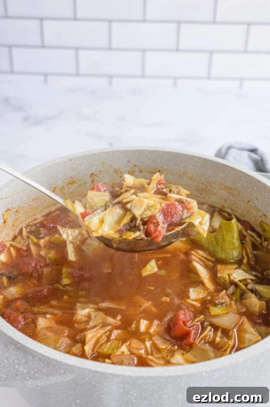 A ladle holds a large portion of savory unstuffed cabbage roll soup over the full pot, ready to serve.