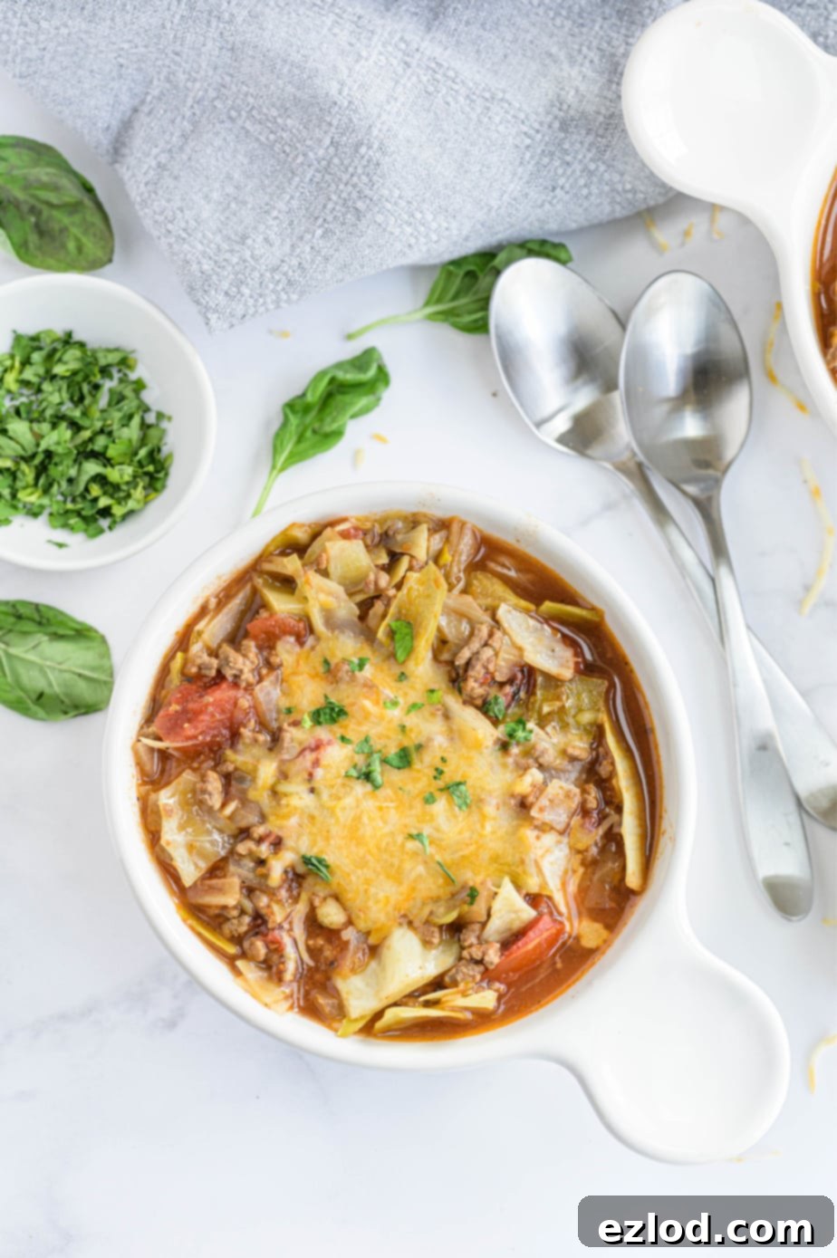 A bowl of unstuffed cabbage roll soup is garnished with melted cheese and fresh basil in a white bowl, ready to be eaten.