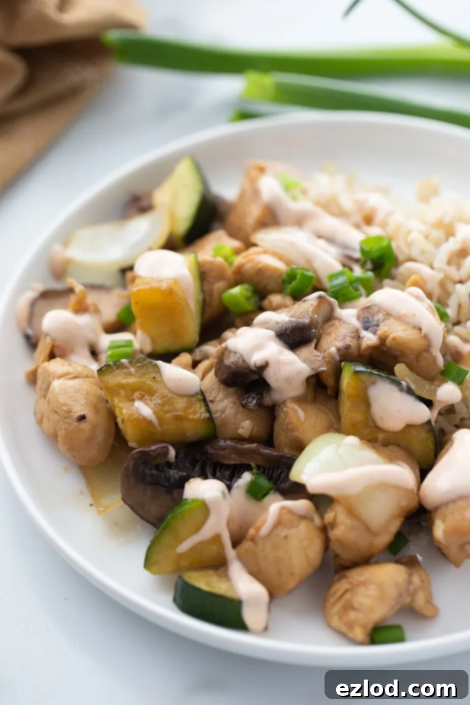 A white plate contains a serving of hibachi style chicken, veggies and rice, drizzled with yum yum sauce.