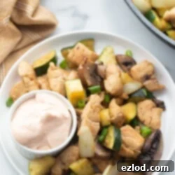 A plate is presented with chicken, veggies, and a small cup of yum you sauce.