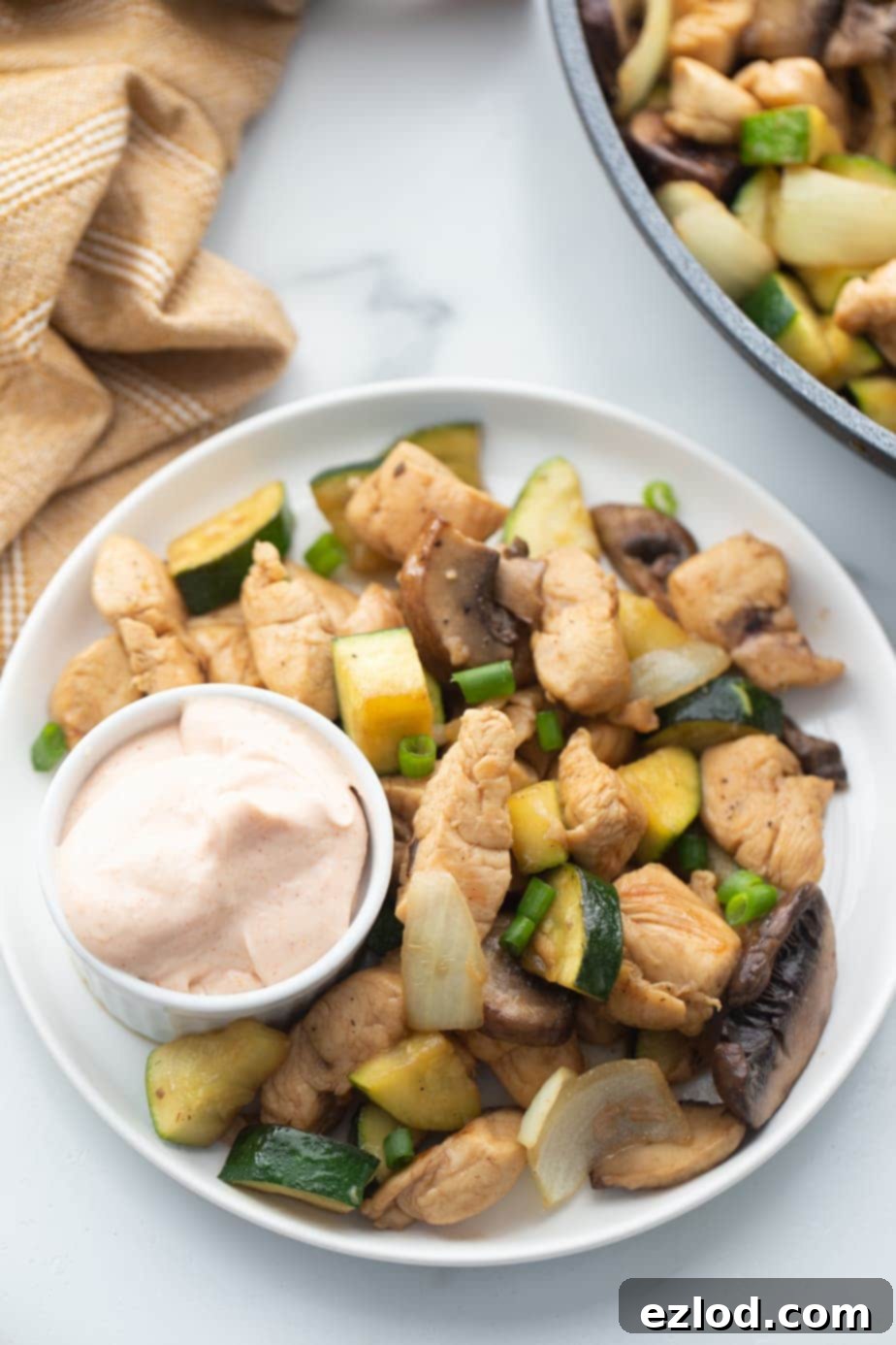 A plate is presented with hibachi chicken, vibrant stir-fried veggies, and a small cup of creamy yum yum sauce ready for dipping.