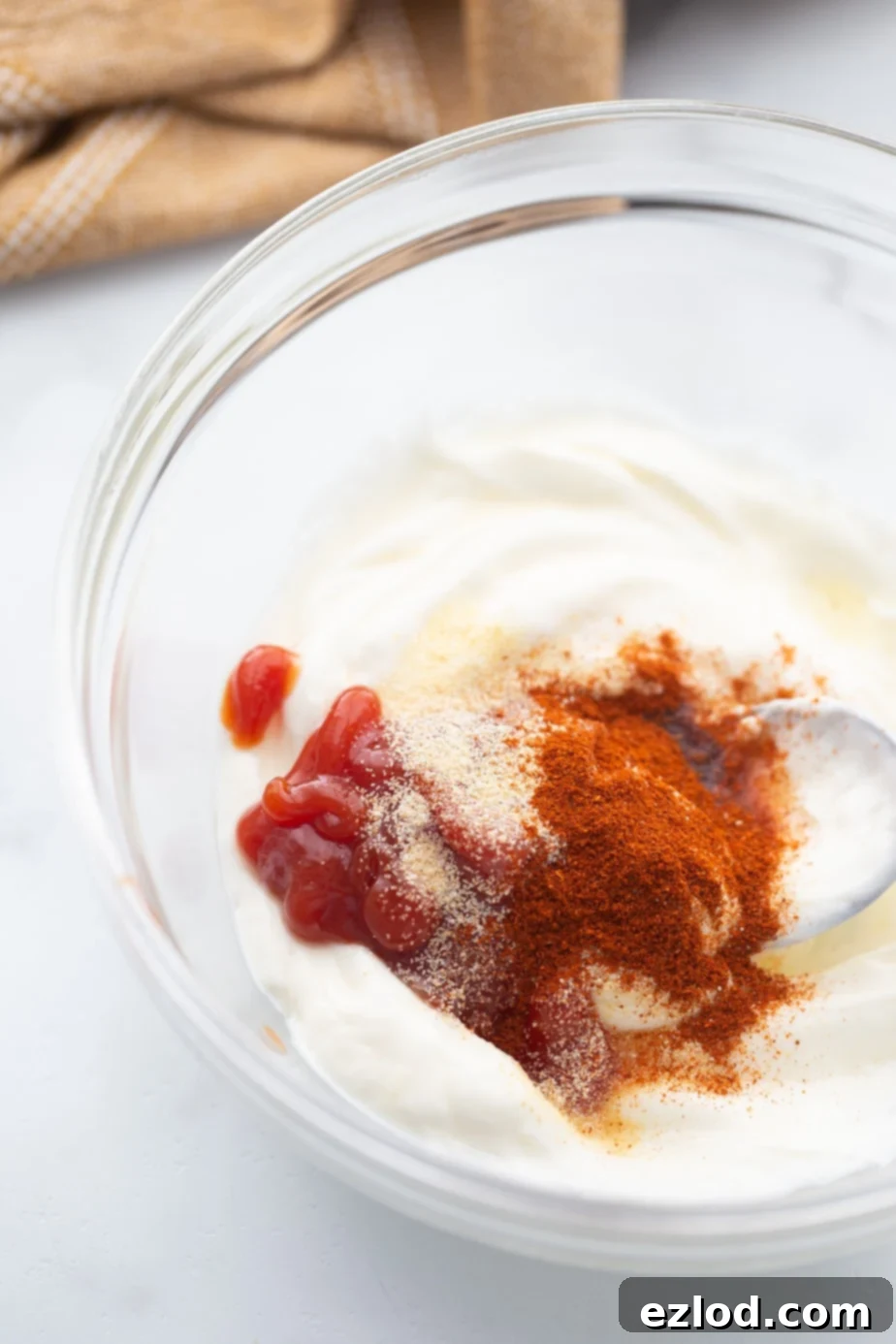 A small glass bowl contains the creamy, pink ingredients for homemade Yum Yum sauce, ready to be whisked together.
