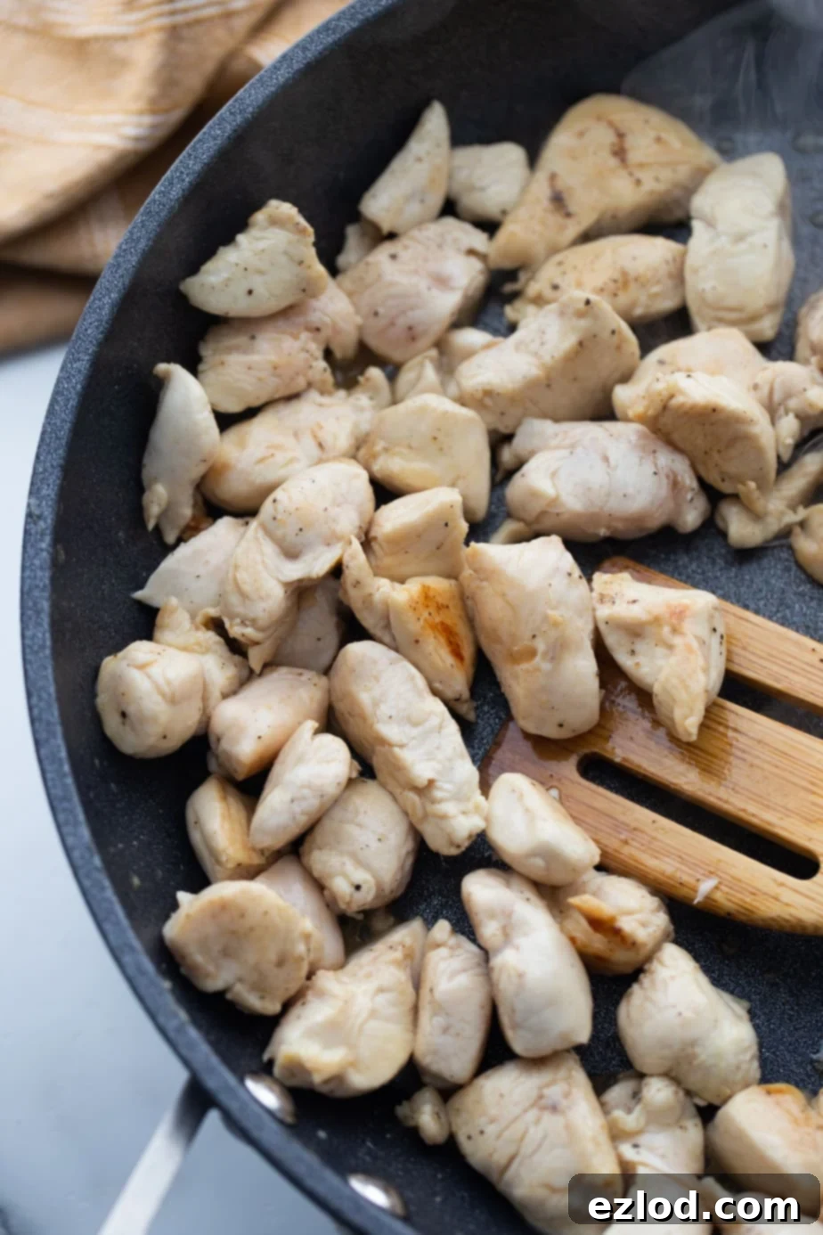 Diced chicken breast is being cooked and browned in a large, hot skillet, ready to be seasoned.