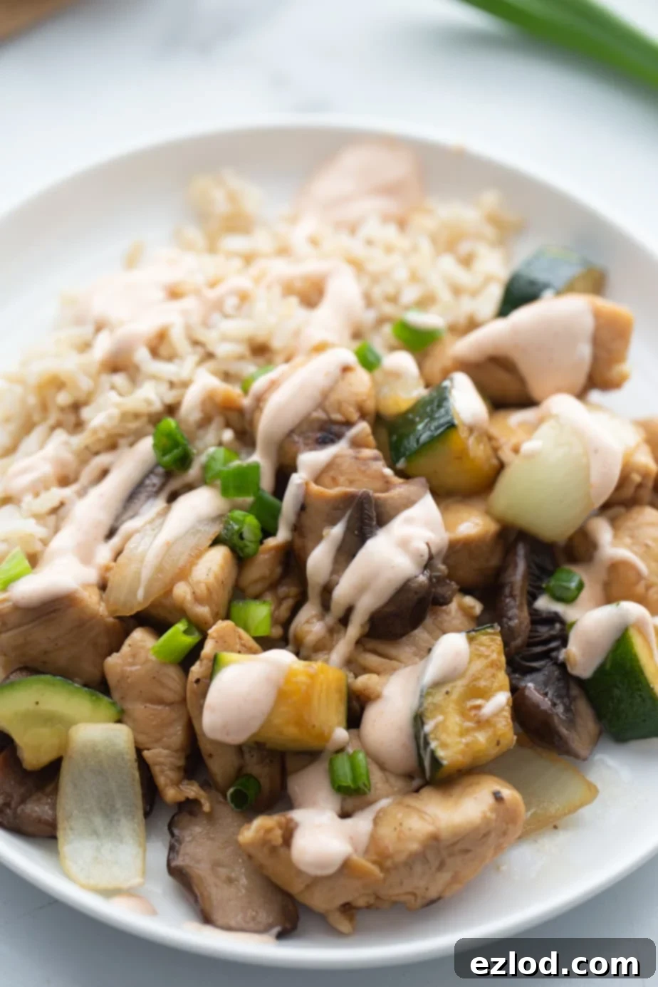 Fluffy white rice and hibachi chicken are drizzled generously with creamy yum yum sauce on a plate, creating a tempting meal.