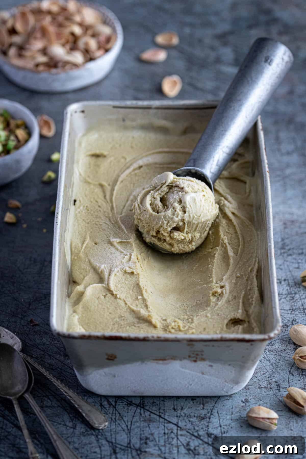 Vegan pistachio ice cream in a metal loaf tin with an ice cream scoop.