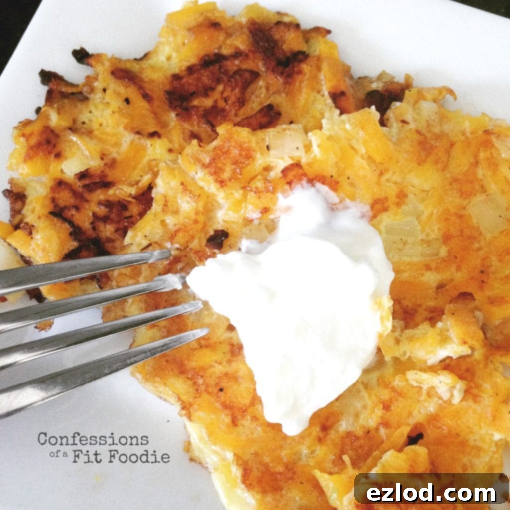 Two golden-brown Butternut Squash Latkes topped with a dollop of creamy Greek yogurt are presented on a pristine white plate, with a fork resting gracefully on the side. The image perfectly captures the healthy and appetizing nature of this dish.
