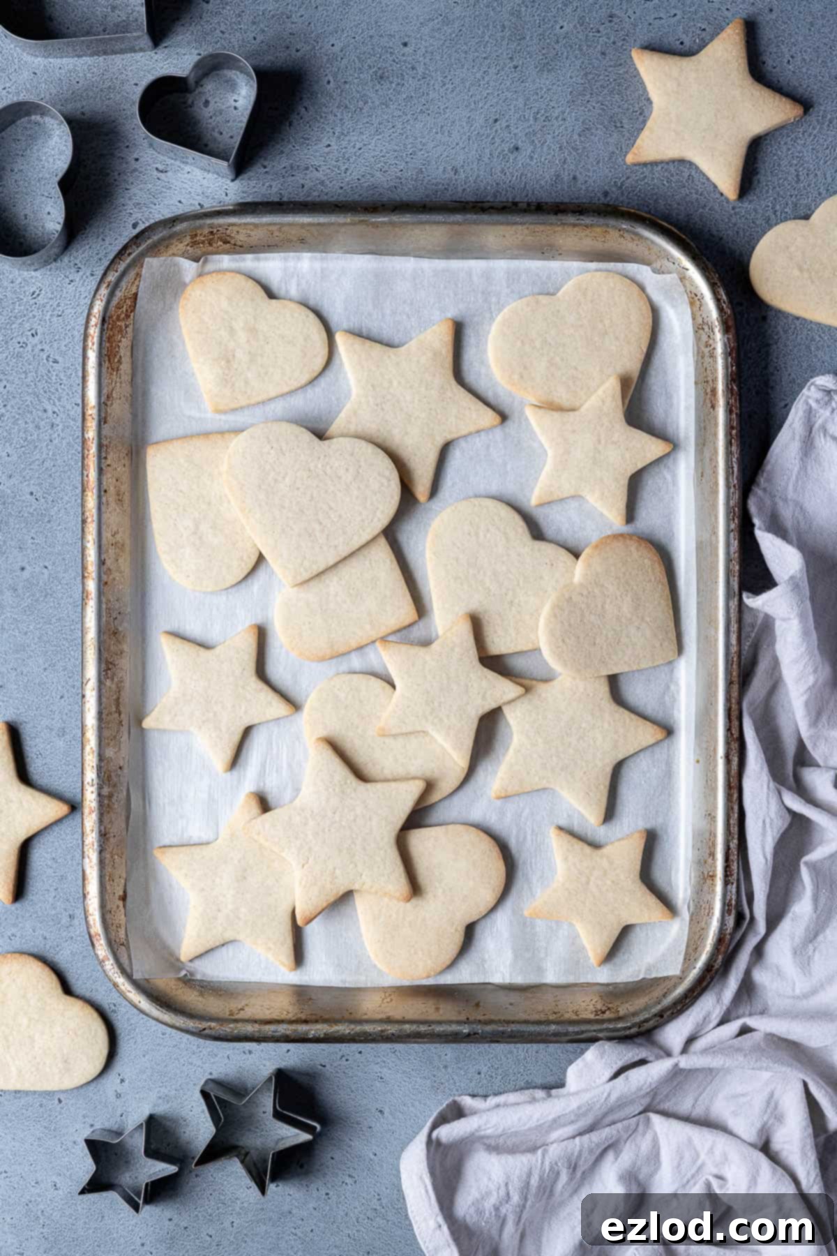 Vegan vanilla sugar cookies on a meatl baking tray with cookie cutters and a grey cloth.