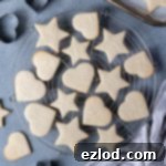 Vegan vanilla sugar cookies on a round wire cooling rack with cookie cutters and a tray of cookies.