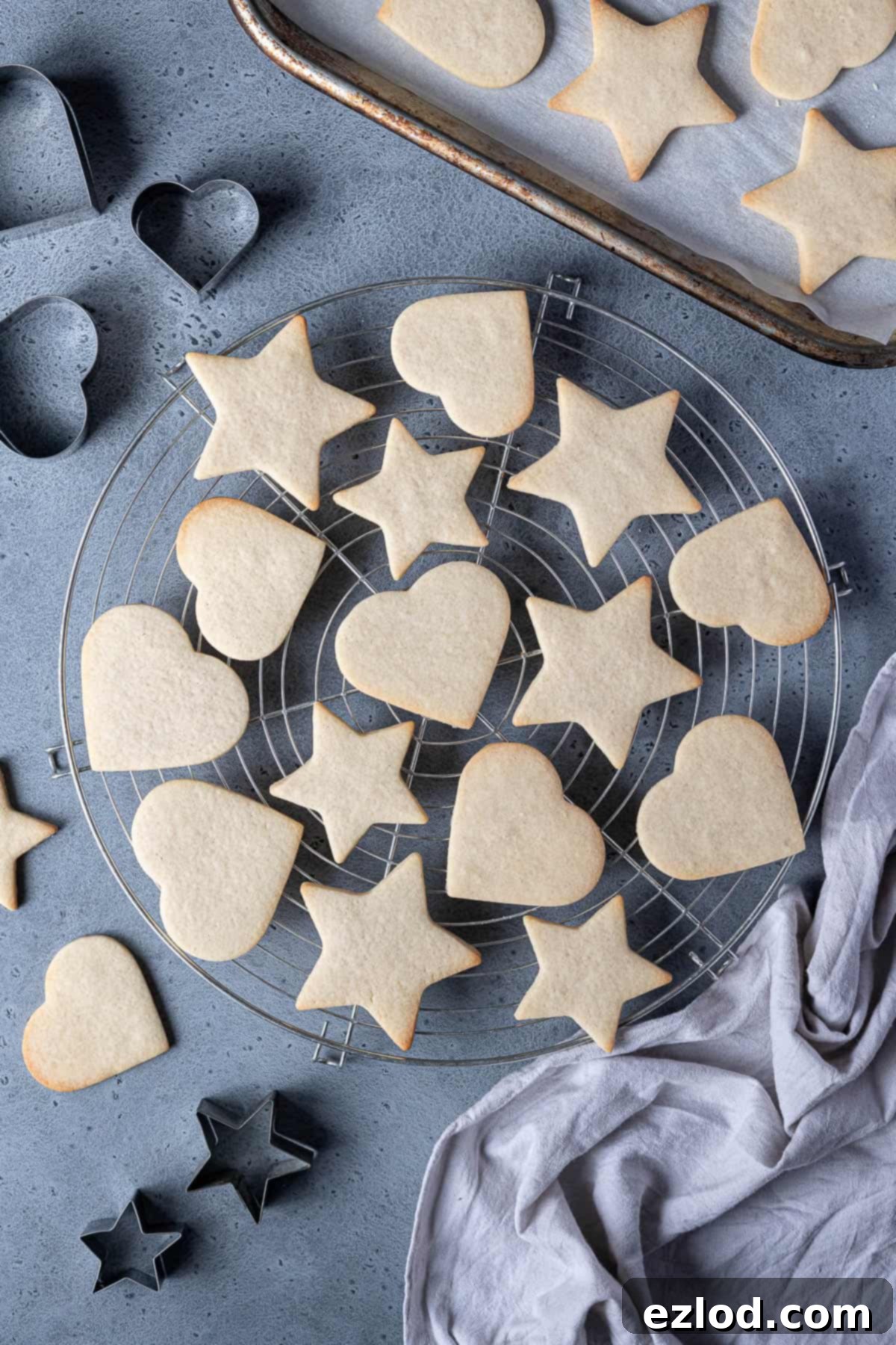 Vegan vanilla sugar cookies on a round wire cooling rack with cookie cutters and a tray of cookies.