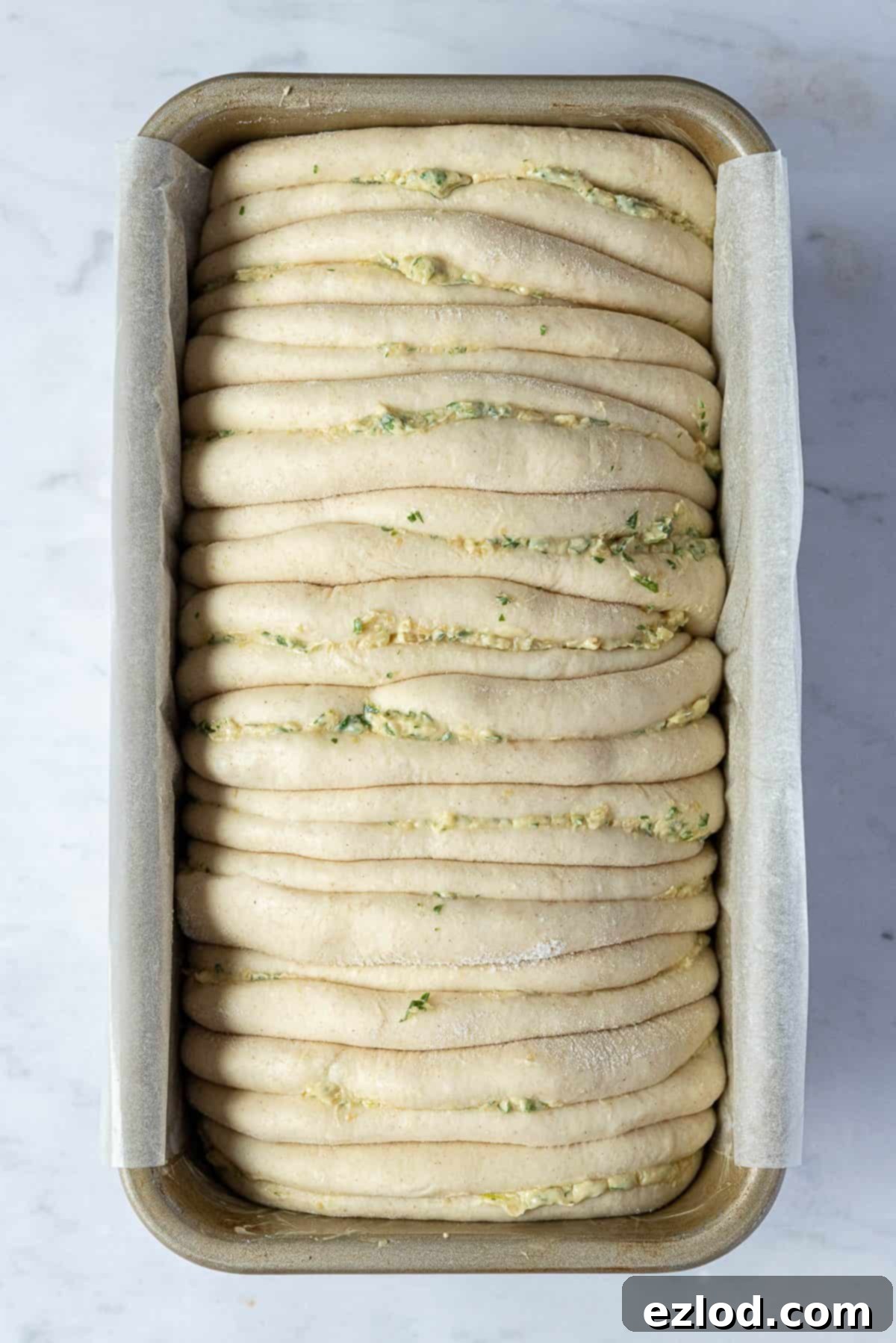 The fluffy, risen vegan garlic pull apart bread loaf in a baking tin, before being placed in the oven.