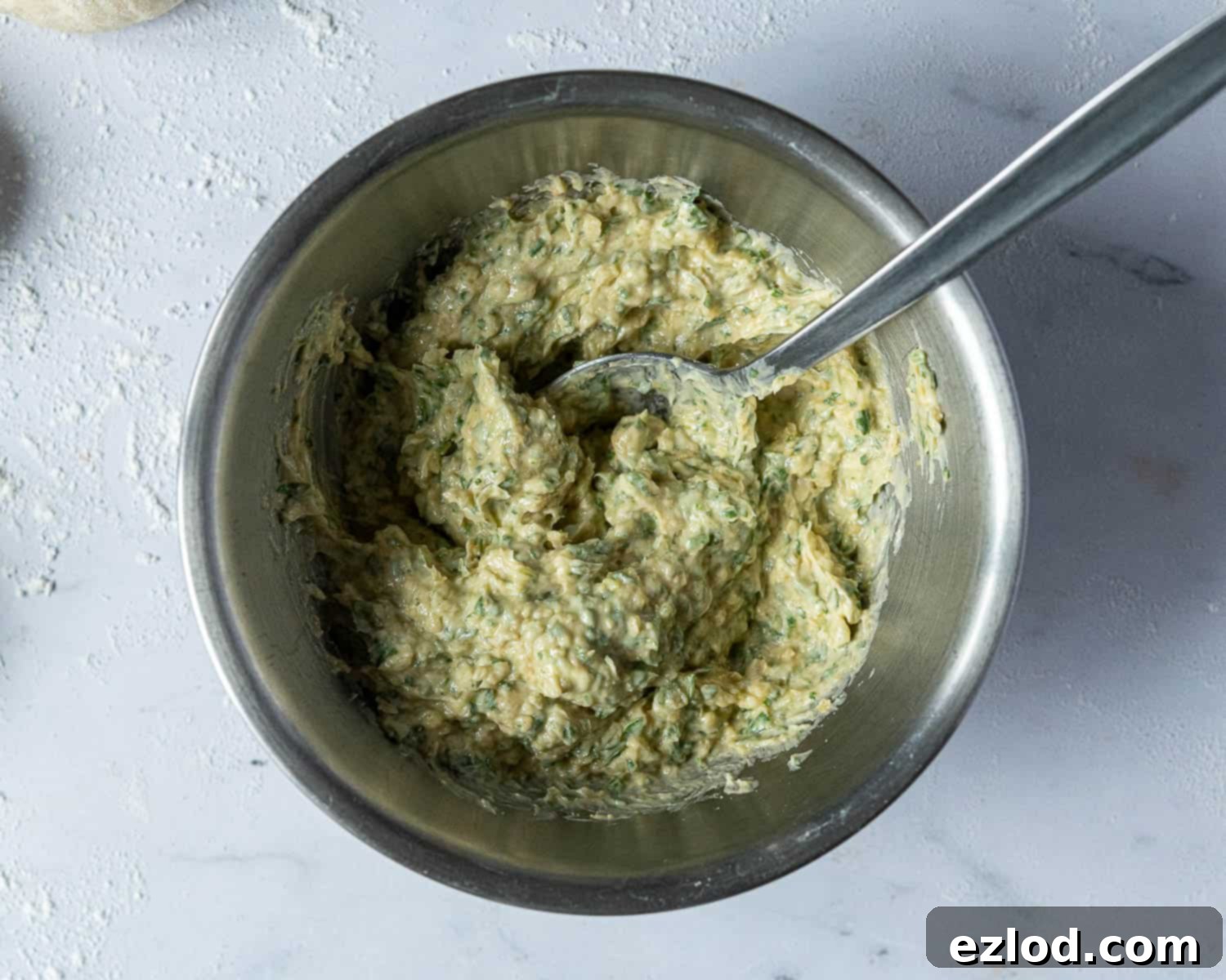 A metal bowl filled with the creamy, green herb garlic butter filling, ready for assembly.