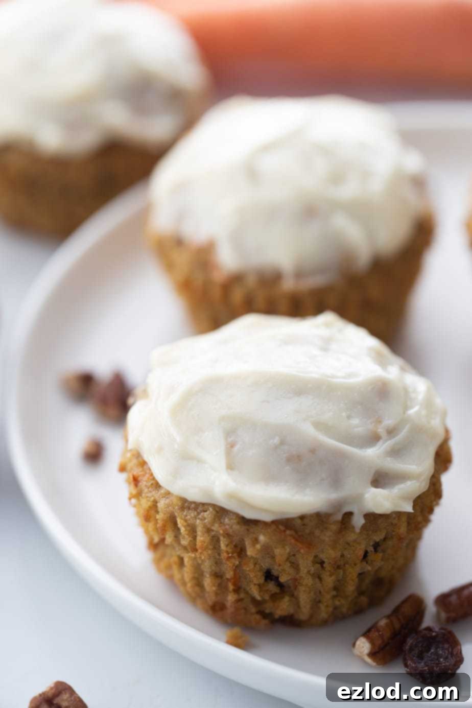 Two carrot cake muffins topped with cream cheese frosting on a white plate