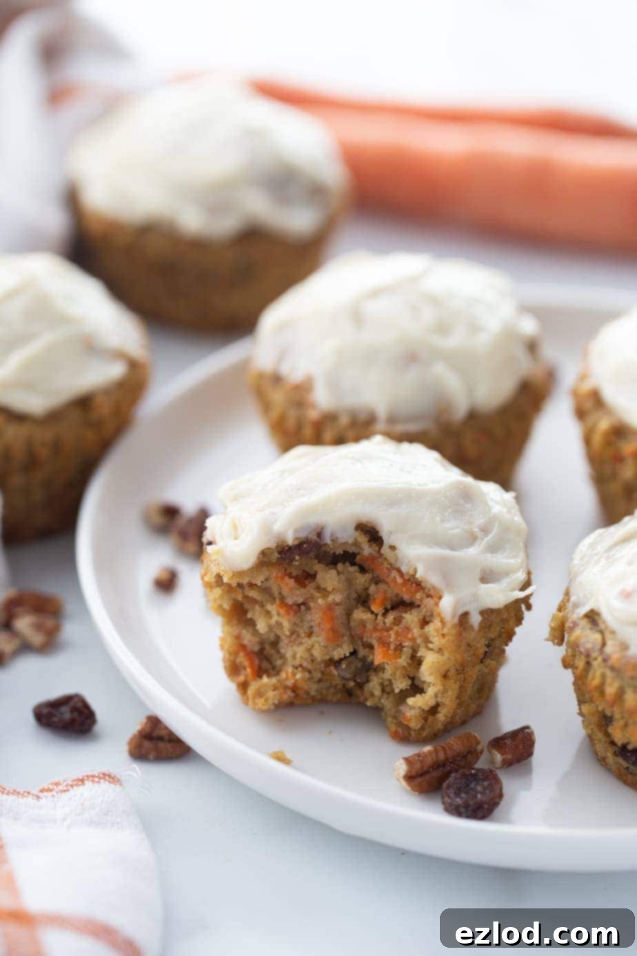 Carrot Cake muffins topped with cream cheese frosting on a white plate. Some cakes are in the background off of the serving plate.