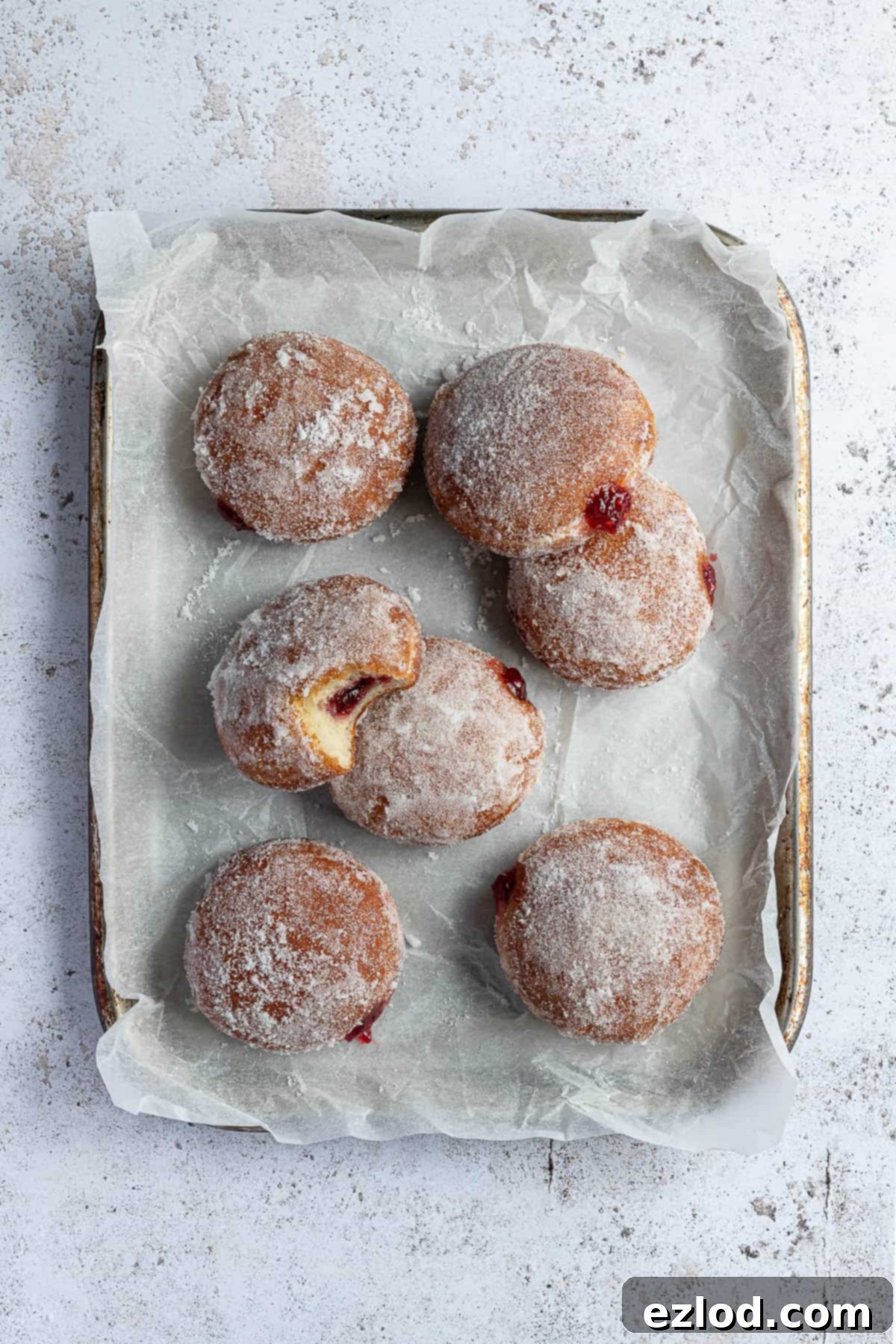 Vegan jam doughnuts on a parchment lined baking sheet.